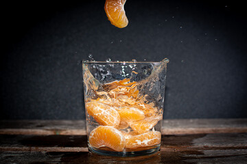 gajos de mandarina con mucha vitanima C cayendo sobre vaso lleno de agua