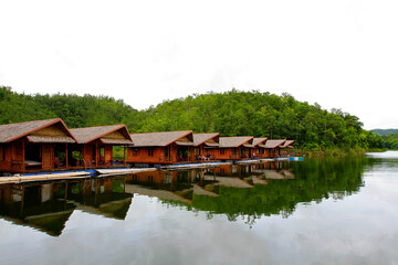 Fototapeta na wymiar Wooden houses floating on river for tourist take rest and chill out among beauty of nature with green plant mountain at Amadard resort, Kanchanaburi, Thailand. Landmark of Asia travel, Exterior design