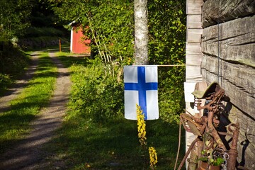 Finnish flag on the wall of the wooden house with picturesque path in the forest on the background. Finland.