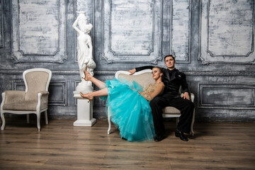 young couple in evening dance costumes posing while sitting on sofa in dance hall