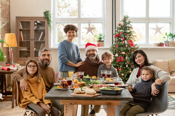 Happy young and mature couples and three cute kids gathered by festive table