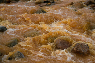 The rapids. Unique yellow river due to the presence of iron mineral in water. Closeup view of the water flowing along the rocky river bed. 