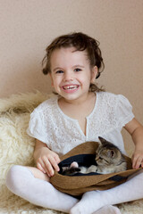 Cute little girl kid plays with a kitten in a hat.