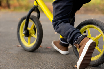 Legs of little boy in casual pants and brown sports shoes riding on balance bike