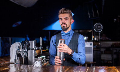 Experienced barman demonstrates the process of making a cocktail while standing near the bar counter in pub