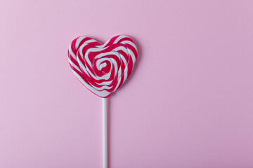 Heart-shaped lollipop and white sweet marshmallows on pink background