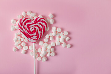 Heart-shaped lollipop and white sweet marshmallows on pink background