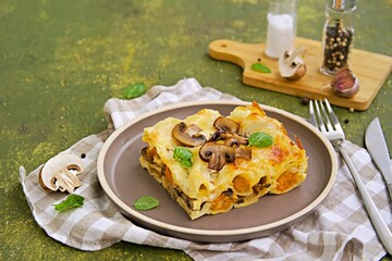 A serving of lasagna with pumpkin and mushrooms on ceramic plate on olive concrete background. Lasagna recipes. Pasta recipes.
