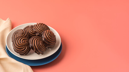 Traditional Russian vanilla marshmallows in chocolate glaze in white and blue plates on pink background. Colorful table and linen textiles. Copy space