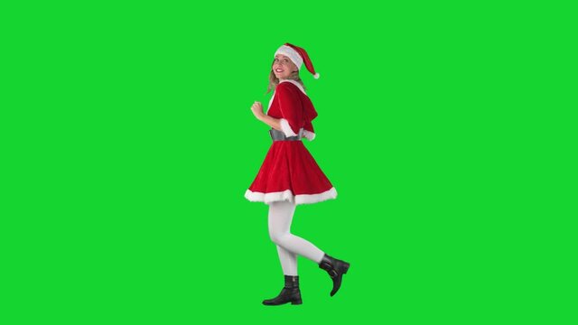 Side view of playful excited jumpy Santa girl dancing while walking. Full body length on chroma green screen. 