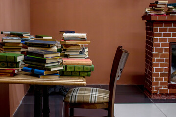 Library. Books in piles on a wooden table, next to the table is a wooden chair.