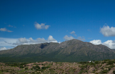 Beautiful view of popular landmark Uritorco hill, valley and green forest under a deep blue sky with clouds in Capilla del Monte, Cordoba, Argentina.