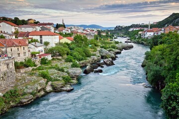 Picturesque view on Mostar city: stone houses on the bank of the Neretva river and mountains in the...