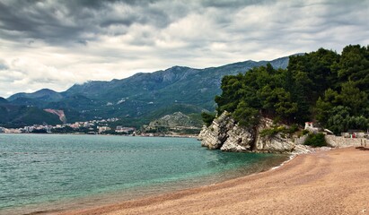 Top view on the green rock on the sandy Royal beach, a city in the lowland and mountains in the background in Milocer, Montenegro.