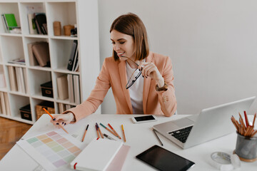 Young positive lady with smile looks at documents. Business woman holding glasses in hands while...
