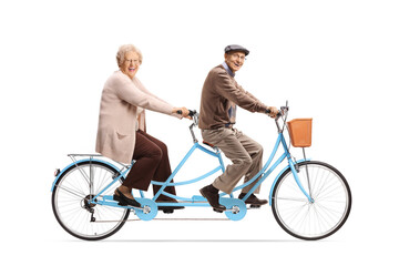 Elderly man and woman riding a blue tandem bicycle and looking at camera
