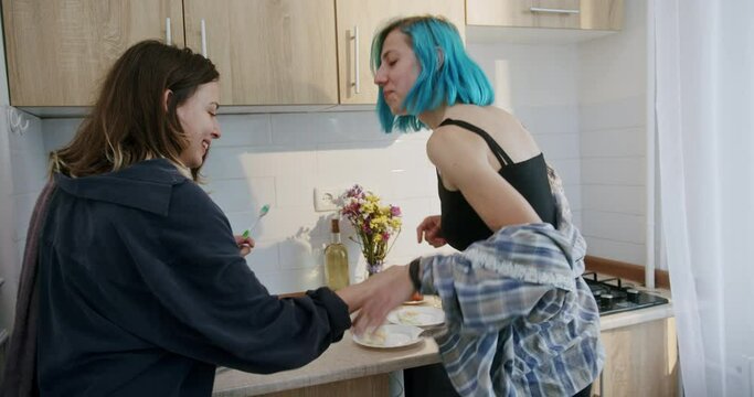 Two gay young woman fooling around in the kitchen before embracing with love hugging each other close