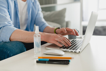 close up focus of spray sanitizer antiseptic at workplace at home working online on laptop person working on laptop on background, stationery - obrazy, fototapety, plakaty