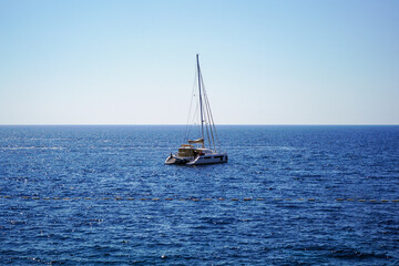 Obraz premium A lone yacht with lowered sails is anchored at sea. Calm sea, sunny day. Rest on a yacht. Sailing. Vacation on a sea yacht. Mediterranean summer landscape. Seasickness.