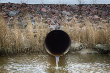 Runoff of excess water through a large-diameter pipe from a water reservoir. In the background is a...