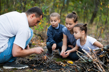 Father showing children how to create campfire in forest when camping