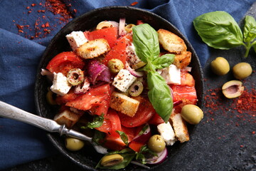 Oriental cuisine. Spicy vegetable salad with spices. Salad of tomatoes, olives, red onions, cheese and basil, croutons on a black cast-iron plate on a black background with red spices. Top view