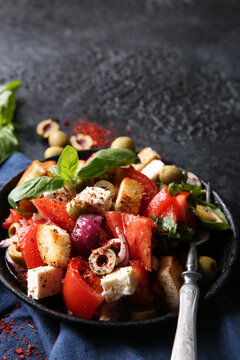 Oriental cuisine. Spicy vegetable salad with spices. Salad of tomatoes, olives, red onions, cheese and basil, croutons on a black cast-iron plate on a black background with red spices. Copy space