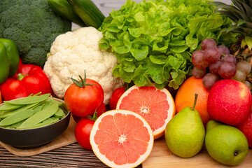Group vegetables and Fruits Apples, grapes, oranges, and bananas in the wooden basket with carrots, tomatoes, guava, chili, eggplant, and salad on the table.Healthy food concept