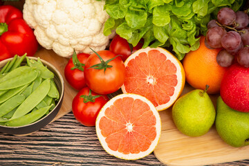 Group vegetables and Fruits Apples, grapes, oranges, and bananas in the wooden basket with carrots, tomatoes, guava, chili, eggplant, and salad on the table.Healthy food concept