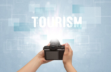 Close-up of a hand holding digital camera with TOURISM inscription, traveling concept