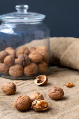 close-up three walnuts. unpeeled and peeled walnuts in shells on a black table and in a glass jar. brown nuts with sackcloth on a dark background. copy space. dried walnut and fruit. vertical