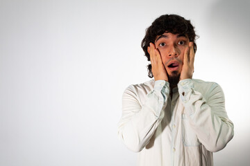 Young Hispanic man wearing casual clothes on a white background with a shocked expression