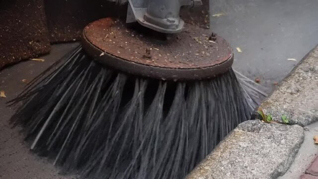 Street sweeper machine cleans town street with brushes. Equipment for cleaning streets and road surfaces. Cleaning Machine brush removing yellow fallen leaves from the autumn street. 