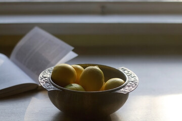 Silver antique bowl with lemons and open book on the table. Selective focus.