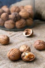 close-up three walnuts. unpeeled and peeled walnuts in shells on a black table and in a glass jar. brown nuts with sackcloth on a dark background. copy space. dried walnut and fruit.