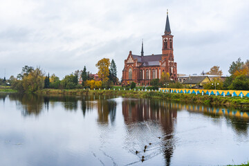 Fototapeta premium Red Catholic Church with Autumn Trees and Pond