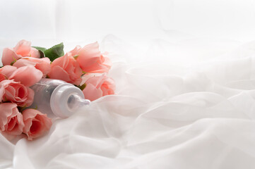 Baby bottle on pink roses bouquet on white soft silk. Selected focus.