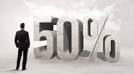Rear view of a businessman standing in front of 50% abbreviation, attention making concept