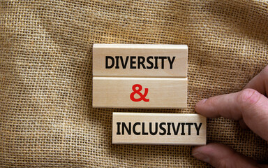 Wooden blocks form the words 'diversity and inclusivity' on canvas background. Male hand. Business, diversity and inclusivity concept.