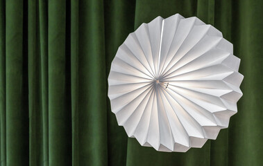 Round corrugated lamp against a background of green curtains.