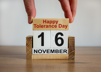 Male hand puts a block with the inscription 'Happy Tolerance Day' on cubes with the date november 16. Beautiful wooden table, white background, copy space.