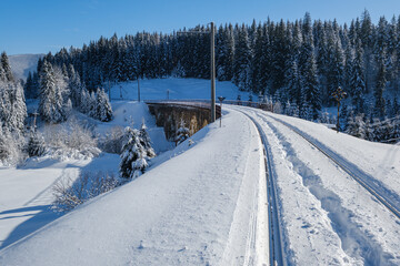 Stone viaduct (arch bridge) on railway through mountain snowy fir forest. Snow drifts  on wayside and hoarfrost on trees and electric line wires.