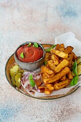 Fried potatoes (deep fried) with herbs and spices, ketchup, pickles and slices of pickled onion on a plate on a light background. Potato food . Baked potatoes with spices and salt.