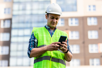 Portrait of a man construction builder in yellow helmet use phone in front of building