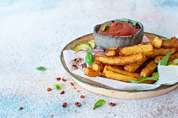 Fried potatoes (deep fried) with herbs and spices, ketchup, pickles and slices of pickled onion on a plate on a light background. Potato food . Baked potatoes with spices and salt.