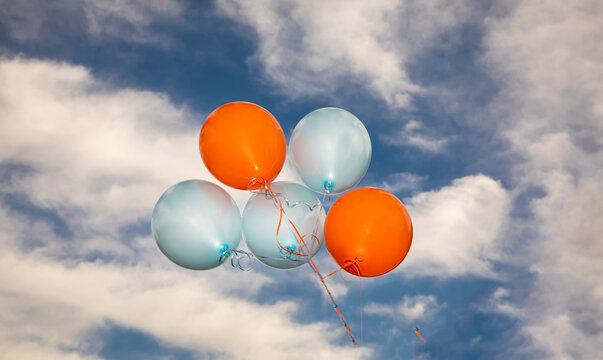 Orange And Blue Ballons Against A Cloudy Blue Sky