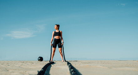 Fit and toned sportswoman working out in functional training gym at the beach - Battle ropes...