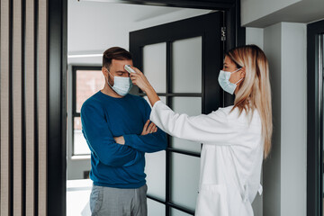 Female doctor using infrared forehead thermometer to check patient's body temperature. They are wearing protective face masks. Pandemic, coronavirus (Covid-19) concept.