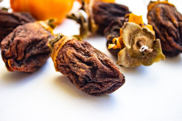 Chocolate persimmon(Hyakume, a variety of chocolate or Zenji-Maru). Large dried fruit whole, brown-yellow with grooves. Ripe orange fruit in the background. Light background.