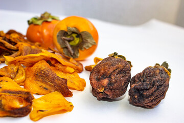 Chocolate persimmon, kinglet. Large dried fruit whole, brown-yellow with grooves. Thin slices, fruit chips. The ripe fruit is orange in color. Light background.